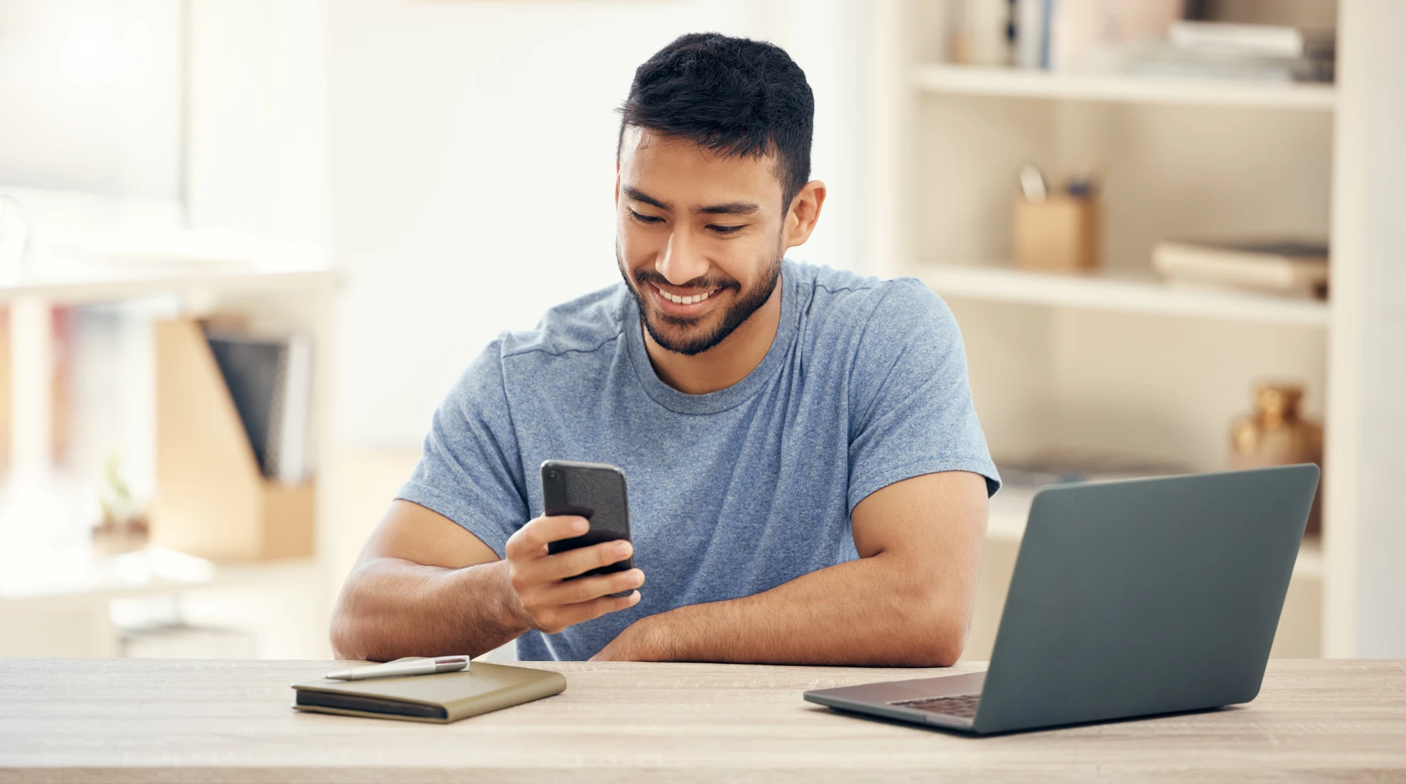 A smiling man looks at his phone while sitting at a desk